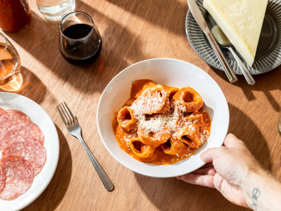 Eine Hand an einem Teller mit Ravioli auf einem eingedeckten Tisch mit Wein und Antipasti