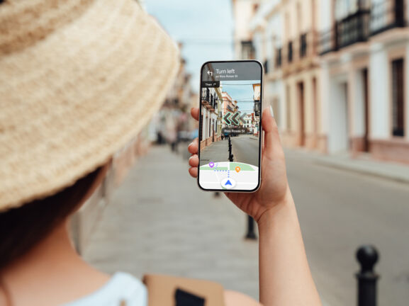 Eine Frau navigiert mit Blick auf ihr Smartphone per Live View von Google Maps durch eine Straße.