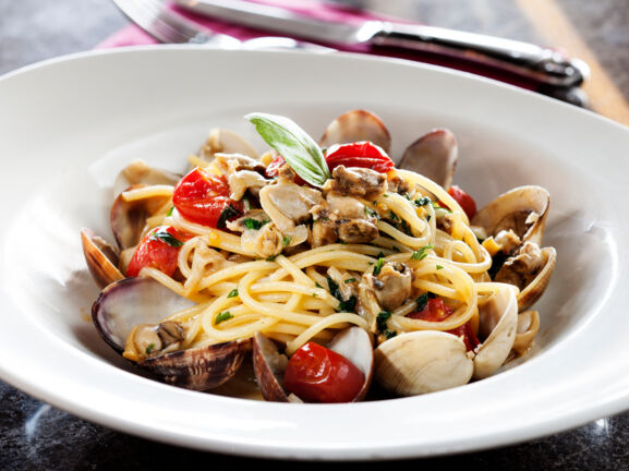 Nahaufnahme einer Portion Spaghetti mit Muscheln und Kirschtomaten auf einem weißen Pastateller.