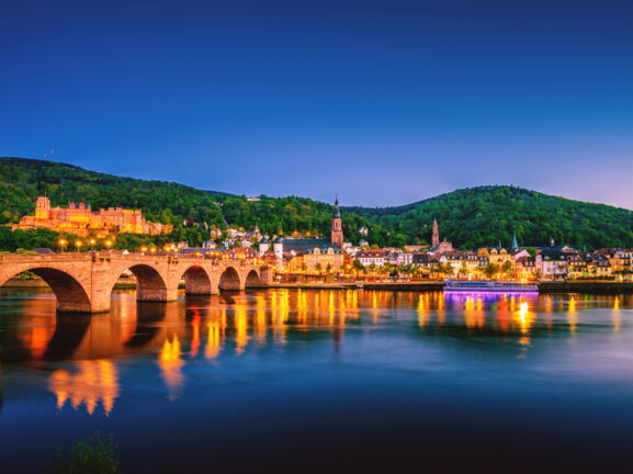 Blick auf die Heidelberger Skyline bei Nacht mit dem Neckar und der Alten Brücke im Vordergrund.