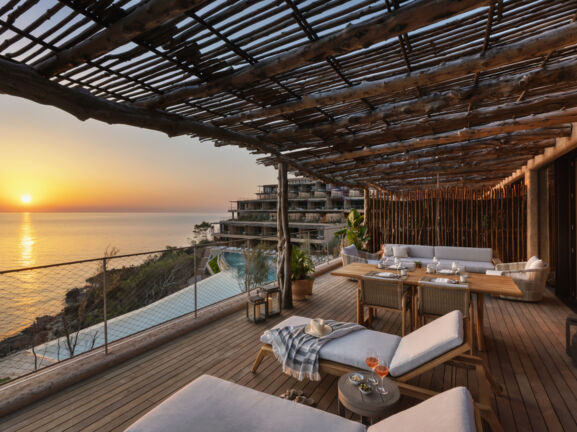 Luxuriöse Hotelterrasse mit Holzpergola am Meer bei Sonnenuntergang.